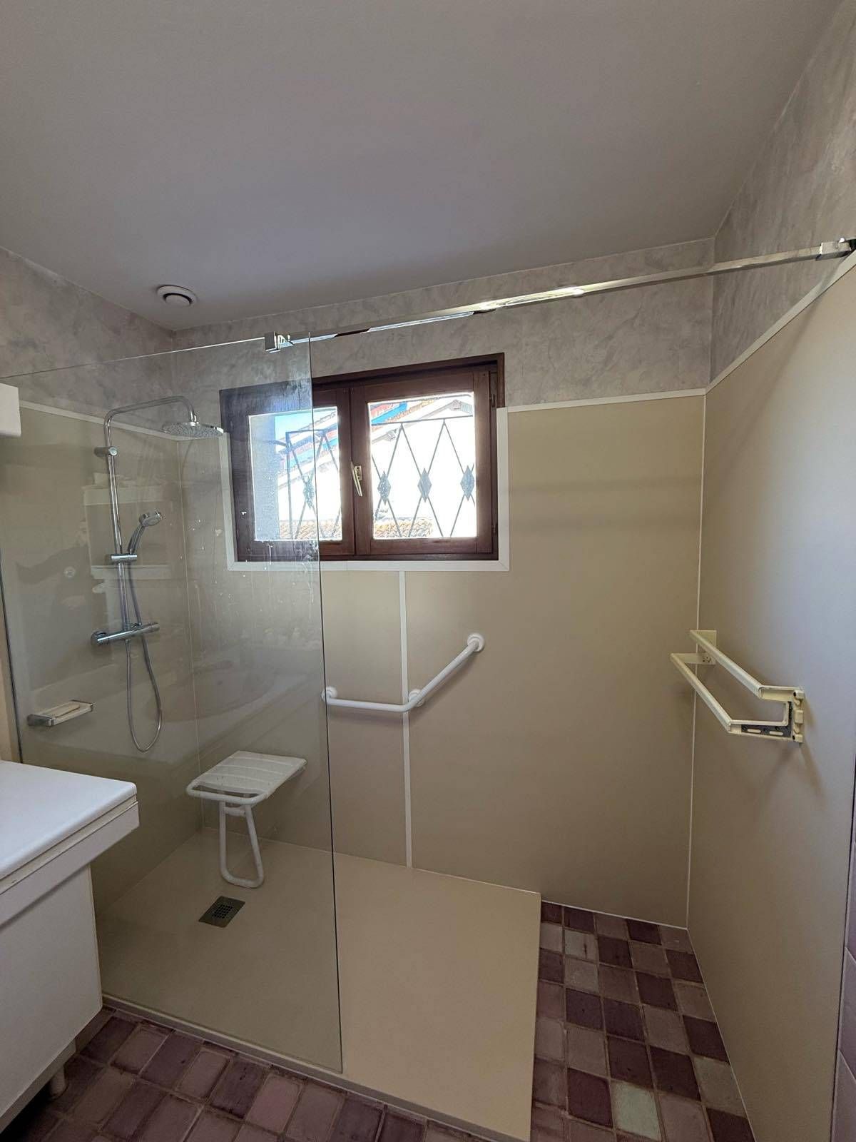 Salle de bain accessible avec douche à l'italienne, barres d'appui, siège de douche et fenêtre