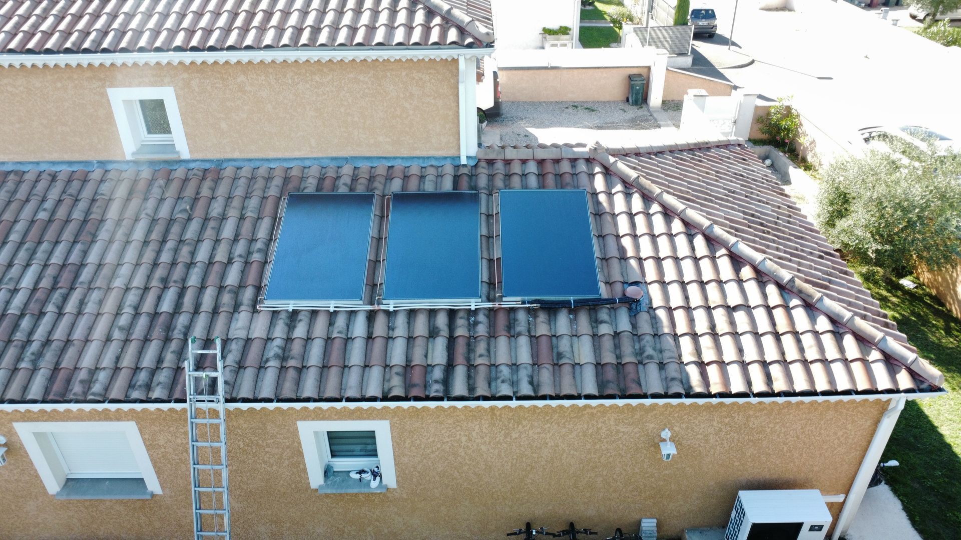 Toiture d'une maison carrelée avec trois panneaux solaires bleus, vue du ciel.
