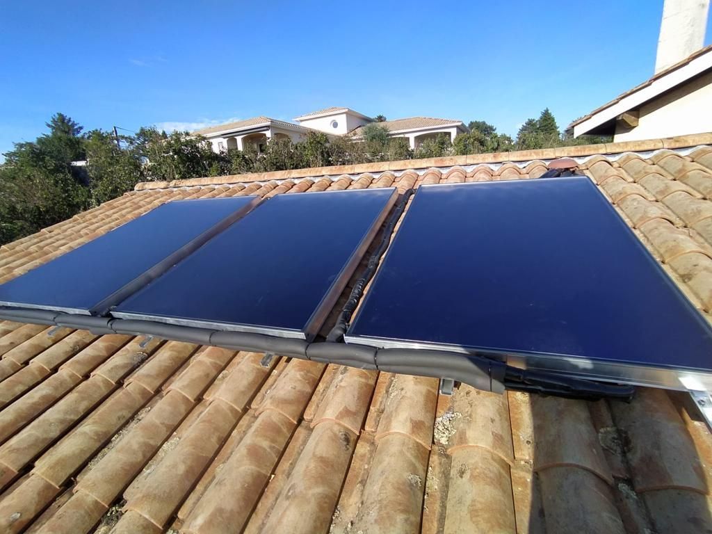 Panneaux solaires installés sur un toit de tuiles offrant une vue sur les montagnes et le ciel bleu.
