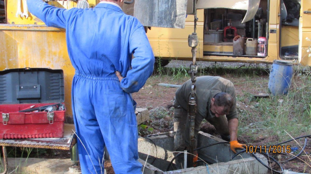 Deux hommes travaillent sur des machines à l'extérieur ; l'un porte une combinaison bleue, l'autre se trouve à l'intérieur d'un conteneur.