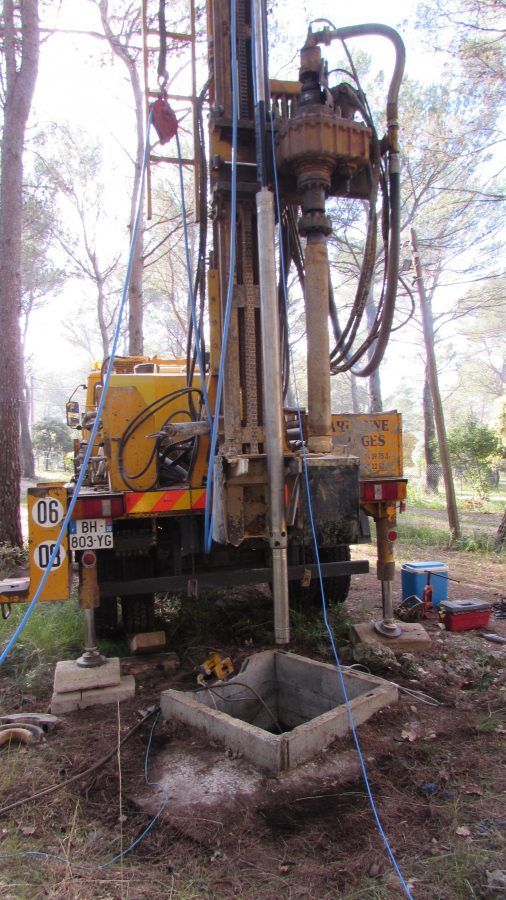Une foreuse jaune, installée sur une dalle de béton dans un décor forestier, est en train de forer un puits.