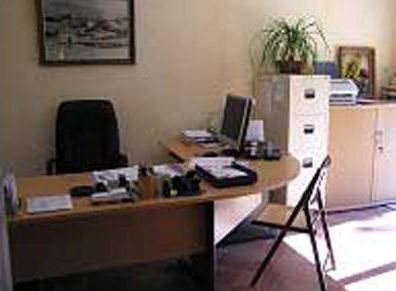 Bureau avec ordinateur, chaise et classeur. Œuvre d'art et plante au mur.