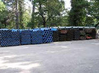 Empilements de tuyaux métalliques bleus et foncés à l'extérieur, arbres en arrière-plan.