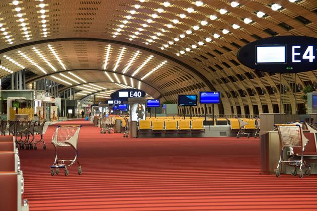 Terminal d'aéroport vide avec moquette rouge au sol, chariots à bagages et panneaux d'entrée sous un plafond voûté