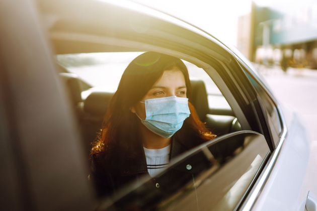 Une personne masquée, assise dans une voiture, regarde par la fenêtre la douce lumière du soleil.