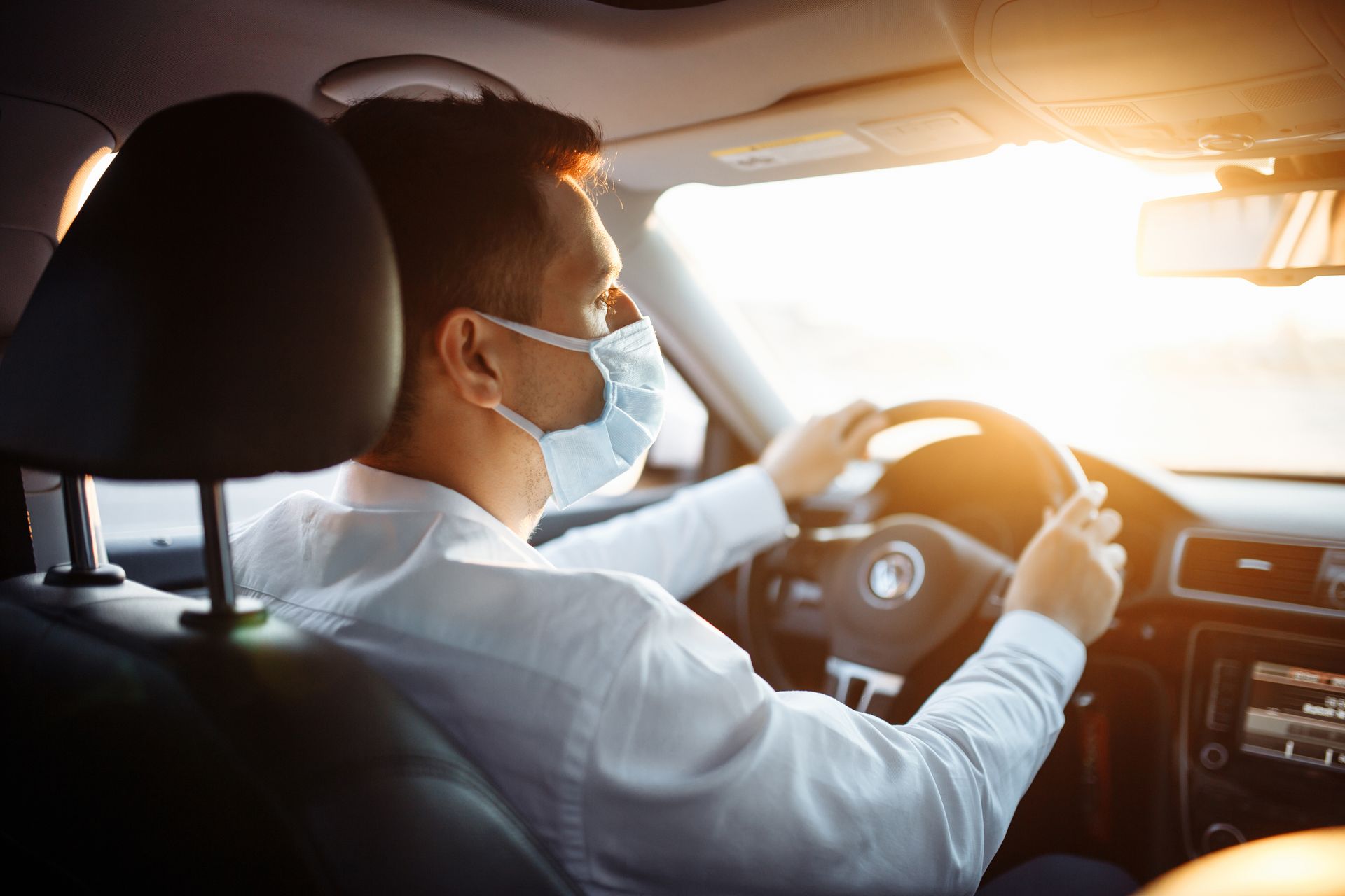 Un conducteur portant un masque conduit une voiture en plein soleil.