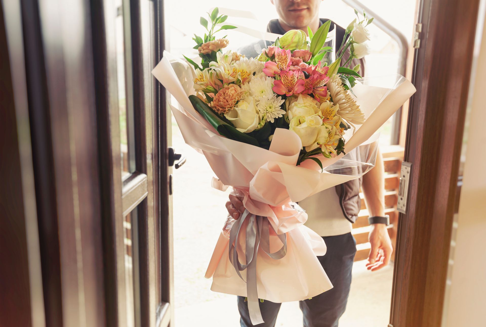 Une personne tenant un grand bouquet de fleurs pastel dans une entrée