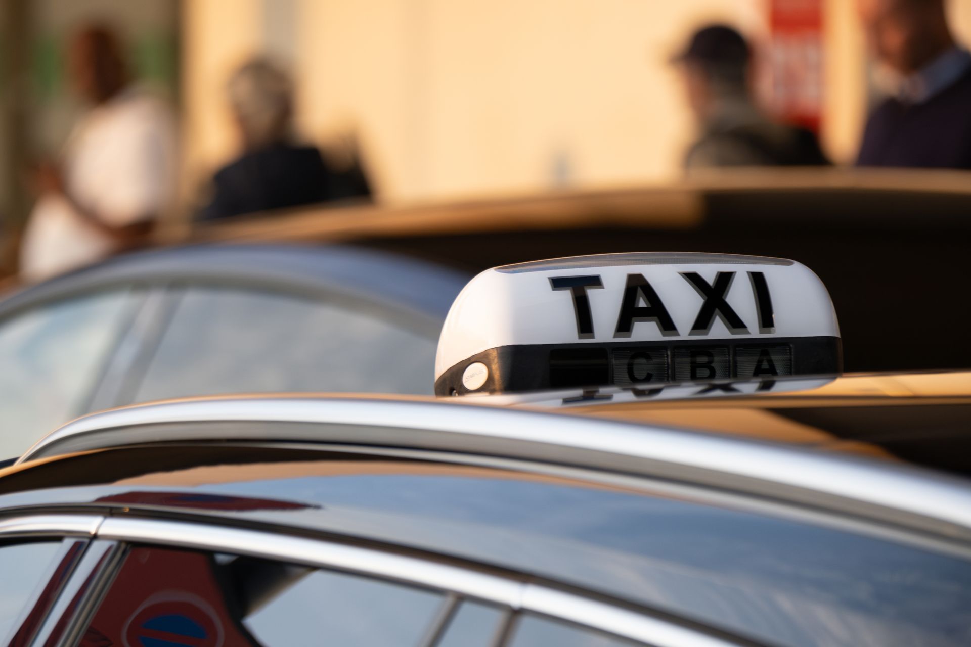 Panneau de taxi sur le toit d'une voiture, avec des personnes floues en arrière-plan.