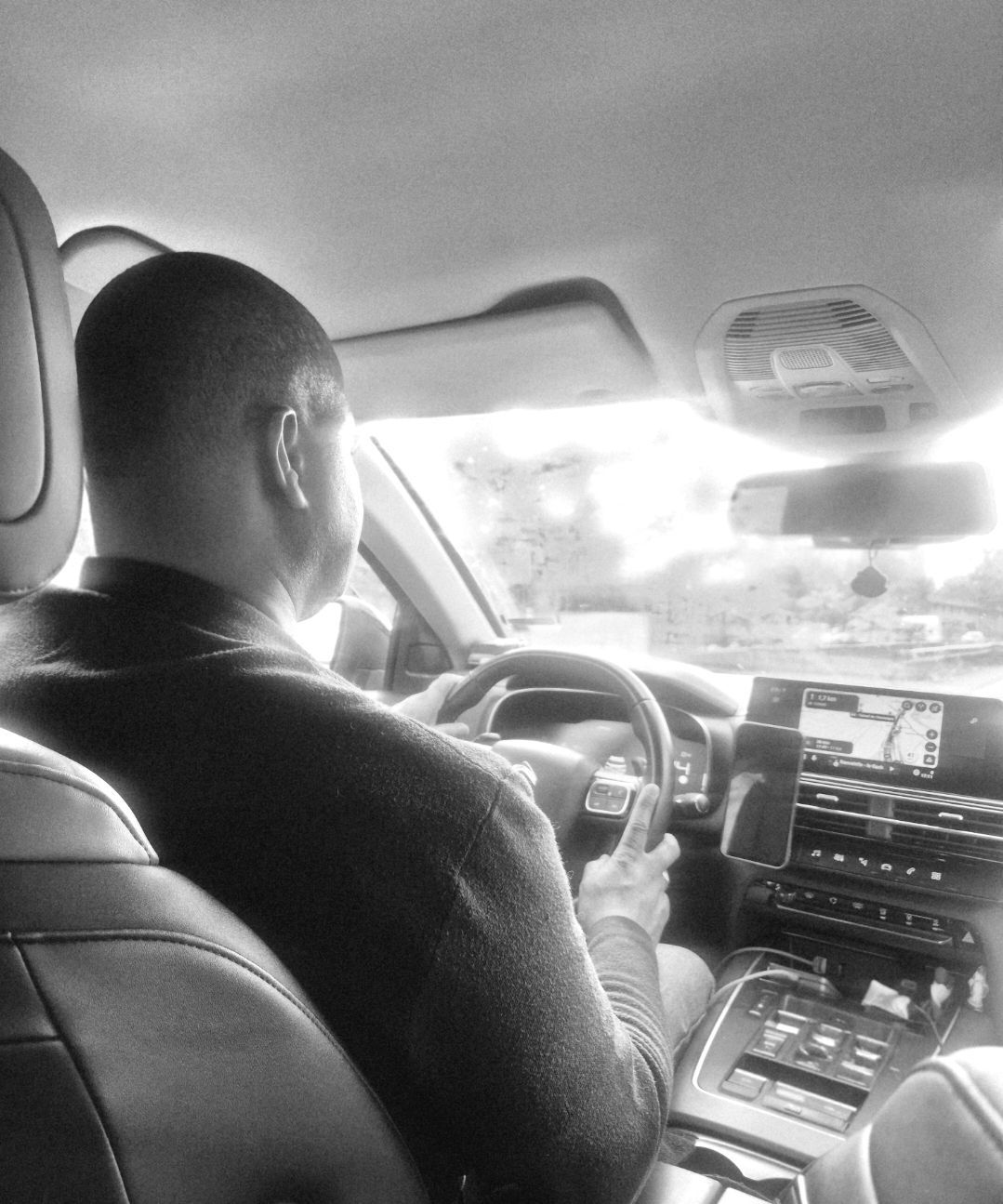 Le conducteur est assis à l'intérieur d'une voiture, tenant le volant, les écrans du tableau de bord visibles.