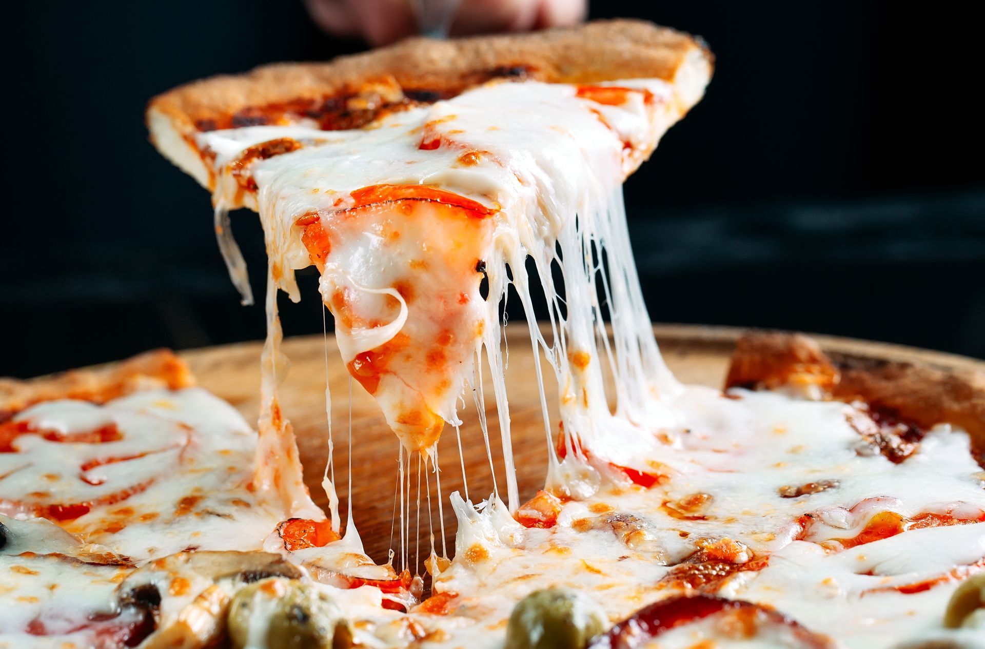Une tranche de pizza soulevée d'une tarte entière, montrant du fromage fondu s'étendant vers le bas.