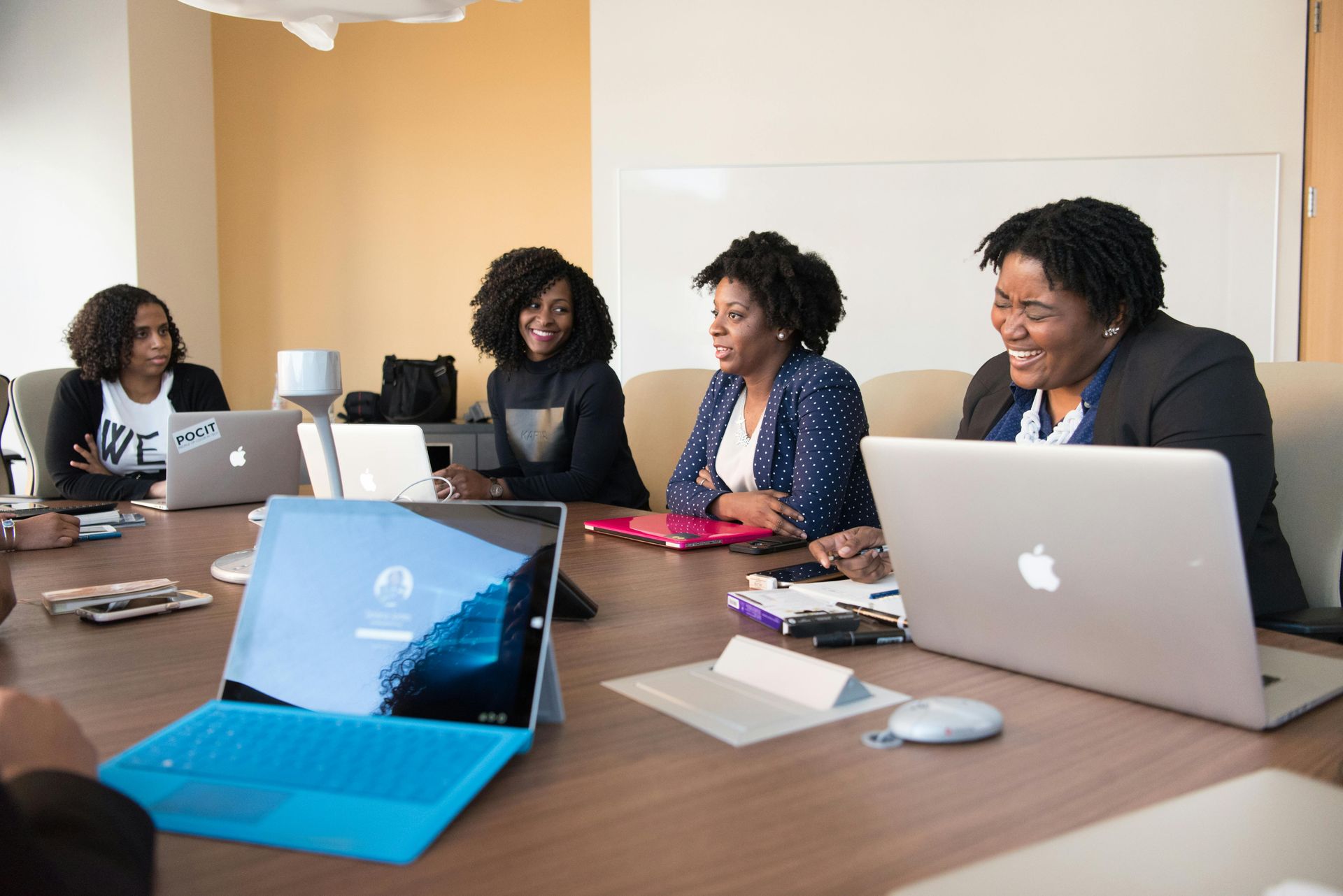 A group of women are sitting around a table with laptops.