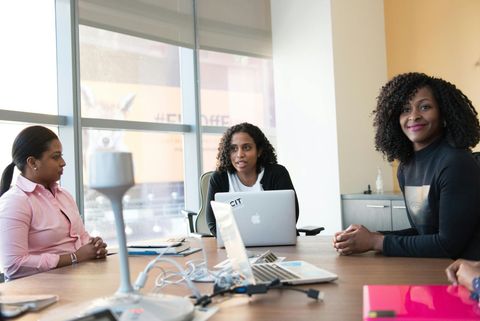 A group of women are sitting at a conference table with laptops.