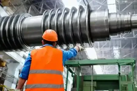 A worker in an orange vest examines a large industrial machine in a factory.