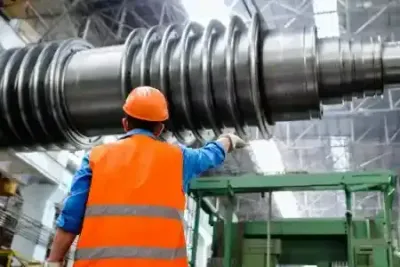 A worker in an orange vest examines a large industrial machine in a factory.