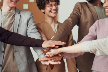 Team of diverse colleagues with hands stacked in a circle, smiling, inside.