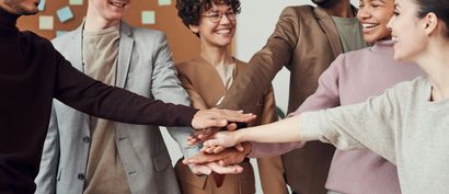 Team of diverse colleagues with hands stacked in a circle, smiling, inside.