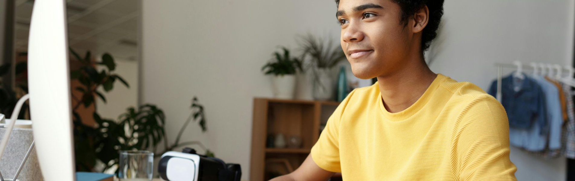 Person in yellow shirt smiling, working at a computer in a light-filled room.