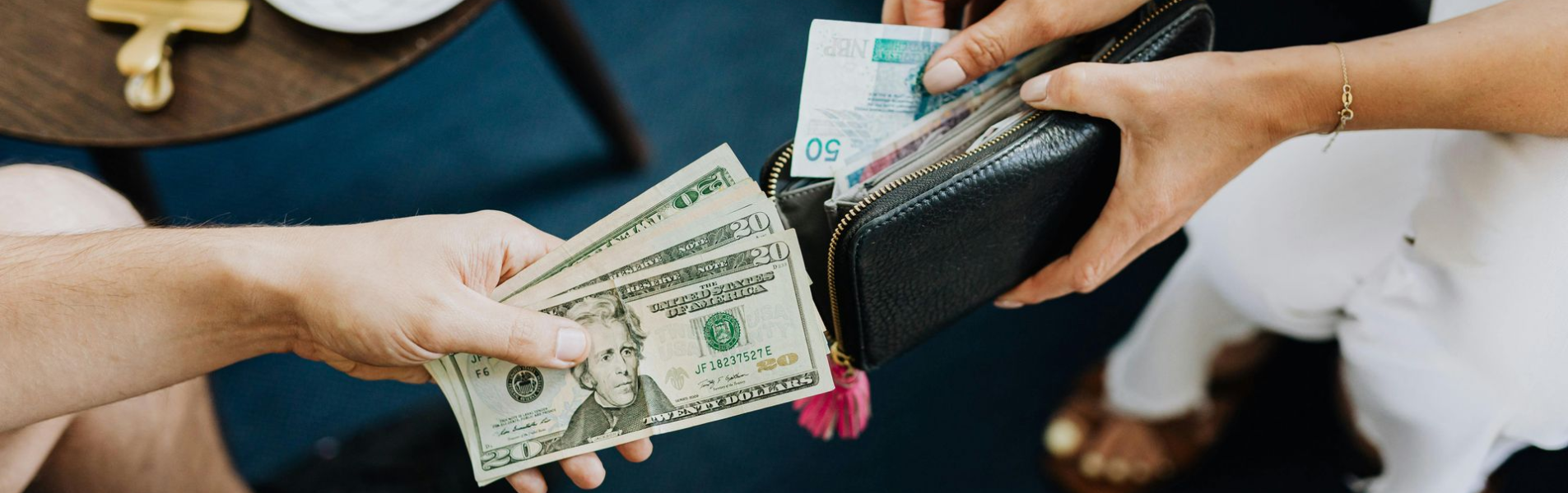 Hands exchanging cash from wallets; coffee cup on table.