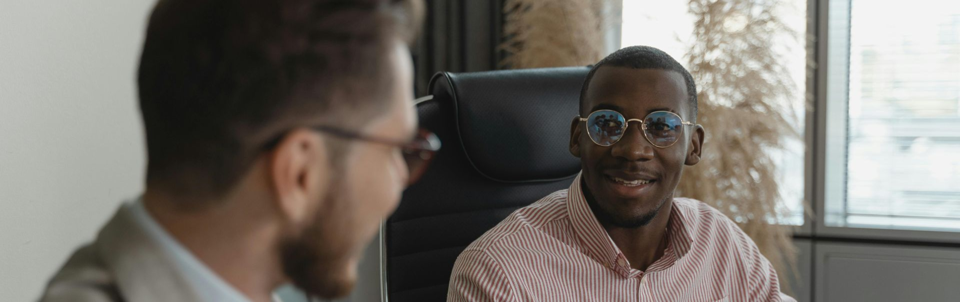 Two men in business attire at a table, one pointing, the other smiles while looking at a tablet.