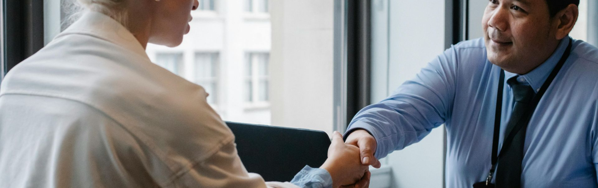 Man in blue shirt shakes hands with a woman in a beige blazer at a desk.