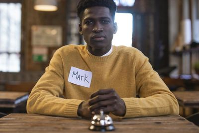 A man in a yellow sweater is sitting at a table with a name tag on his chest.