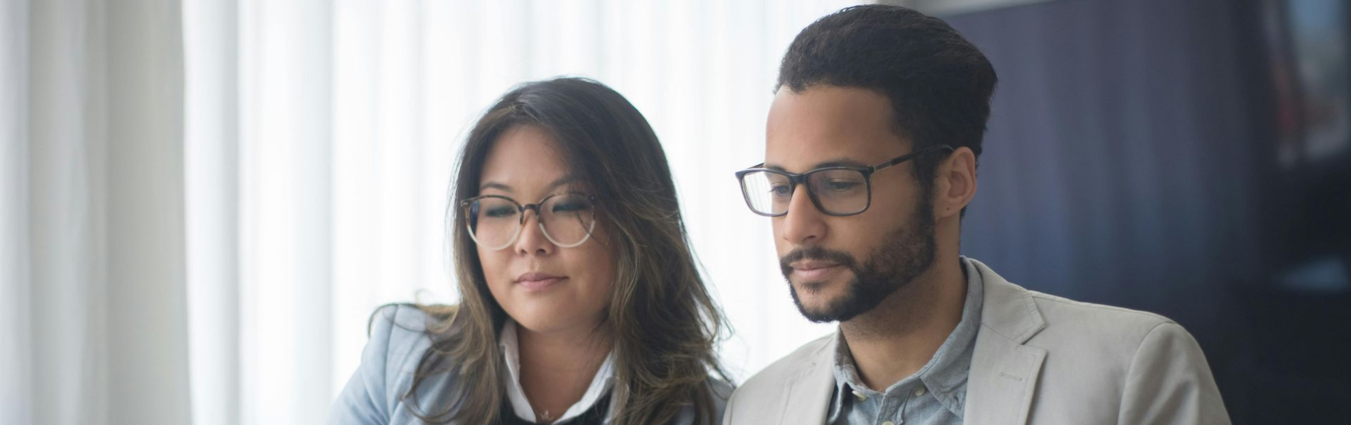 Two people, in business attire, looking at a laptop and documents at a desk in an office.
