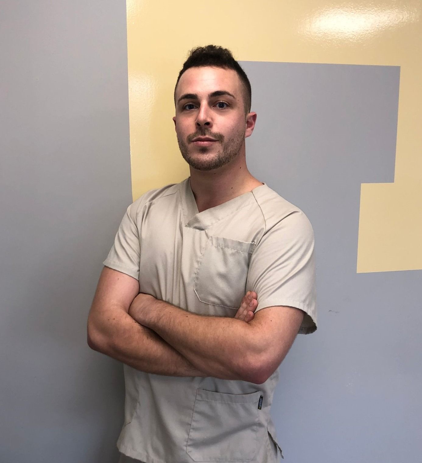 Un hombre con un matorral está de pie con los brazos cruzados frente a una pared.