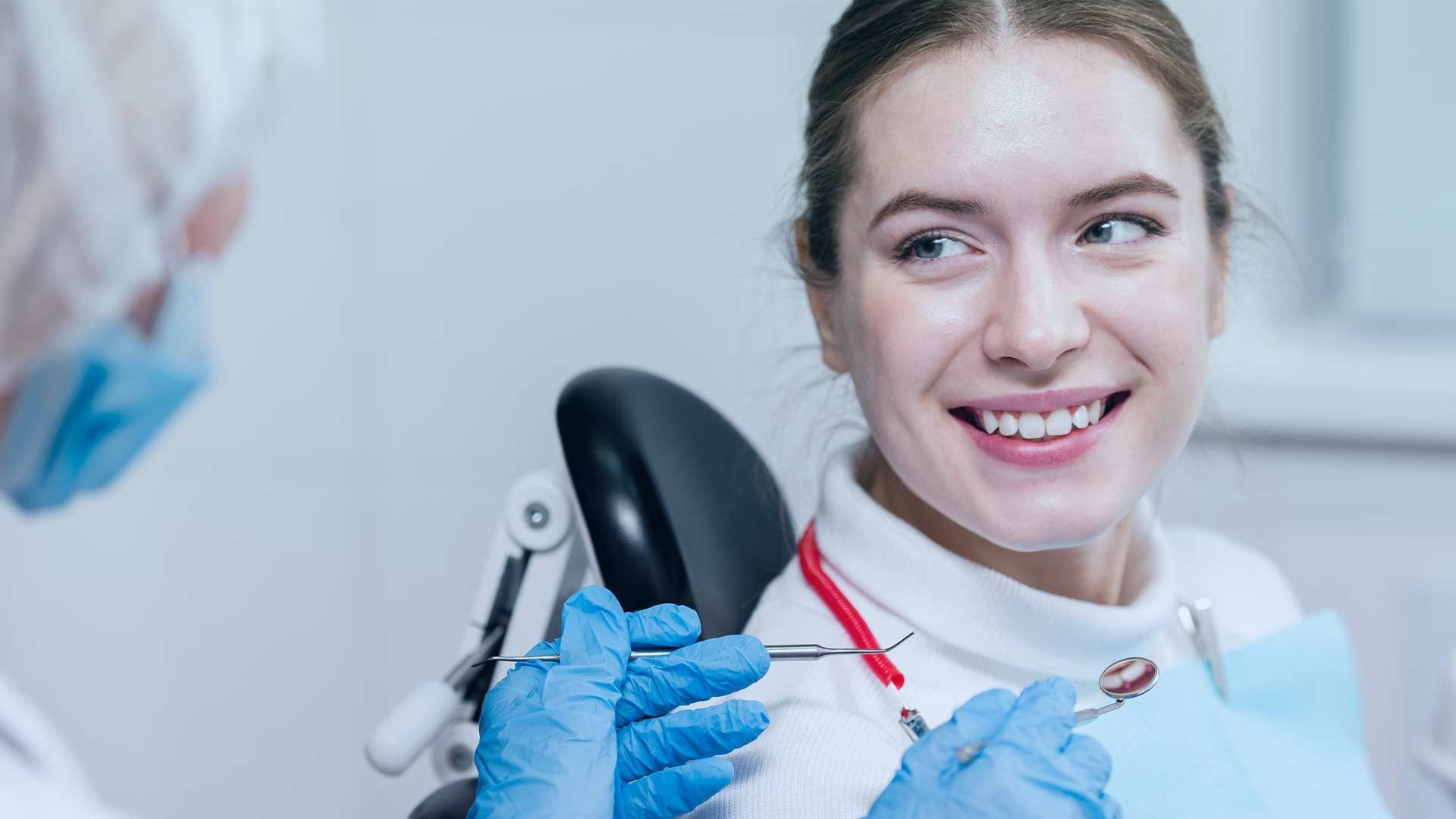 Una mujer está sentada en una silla dental mientras un dentista le examina los dientes.