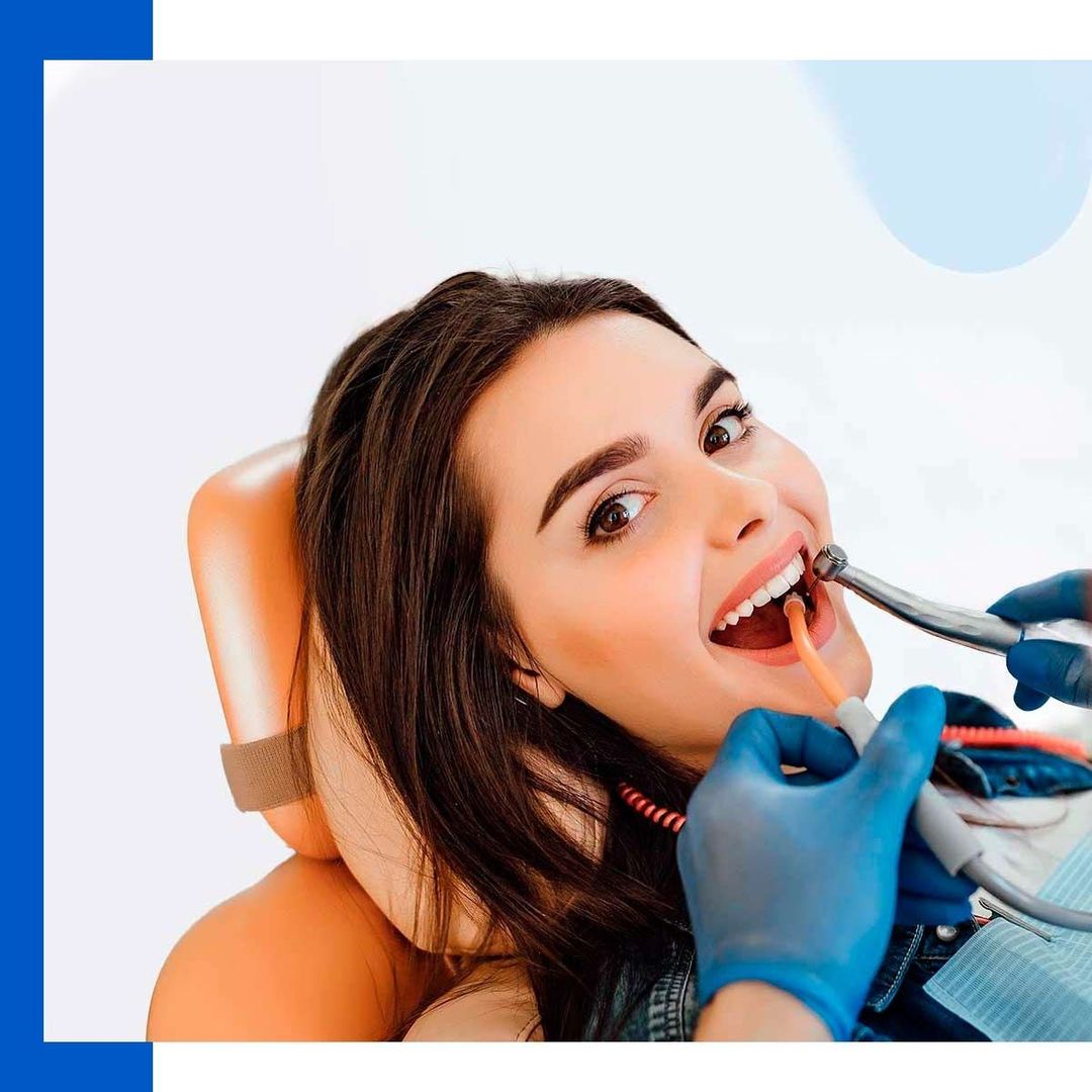 Una mujer está sentada en una silla dental mientras un dentista le examina los dientes.