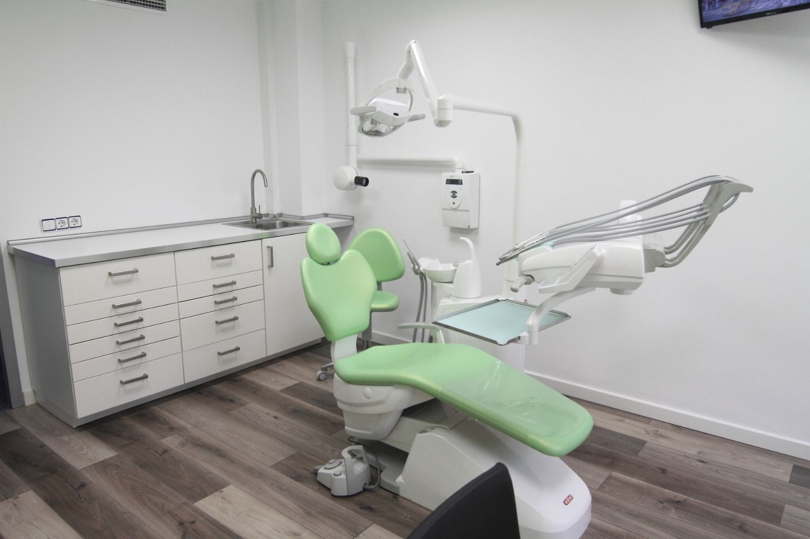 Un consultorio dental con un sillón dental verde y un lavabo.