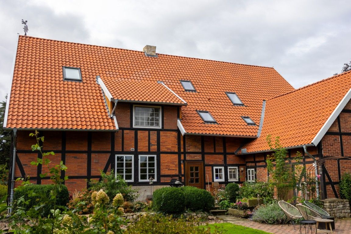 Fachwerkhaus mit frisch gedecktem roten Ziegeldach, mehreren Dachfenstern und angrenzendem Garten.
