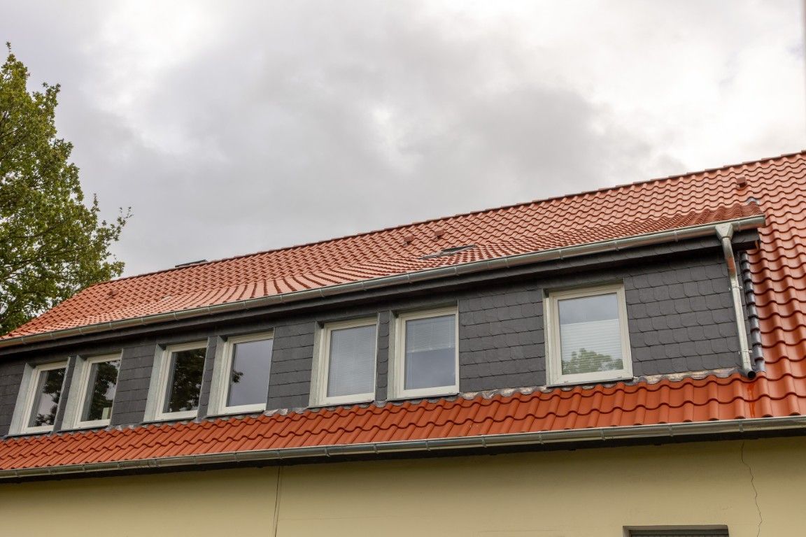 Wohnhaus mit neu eingedecktem roten Ziegeldach und dunkel verkleideten Gauben mit mehreren Fenstern.