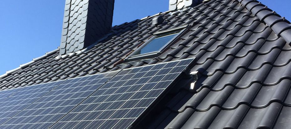 Ein Dach mit Solarmodulen und einem Oberlicht vor blauem Himmel.