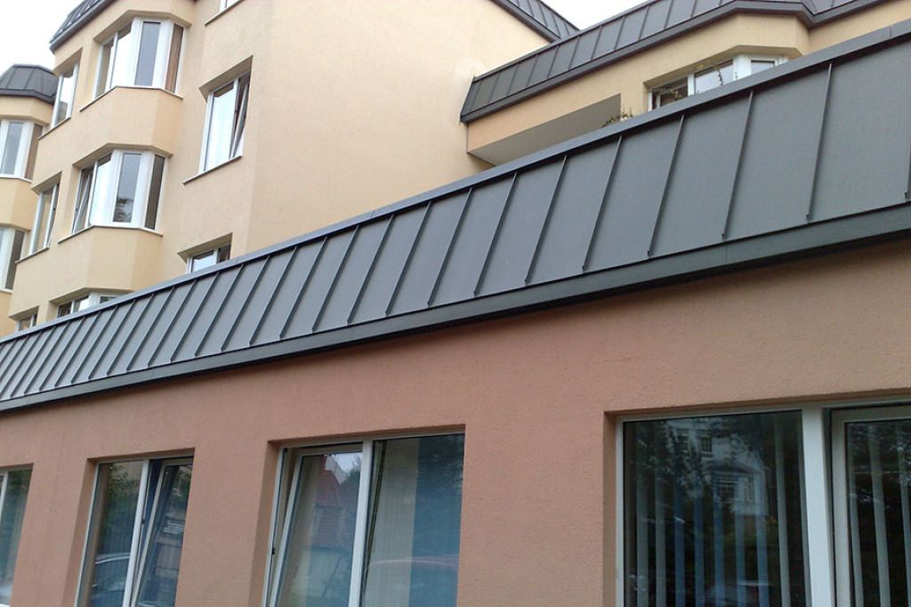Gebäude mit dunklem Metalldach und beige-braunen Wänden. Fenster säumen die Gebäude.