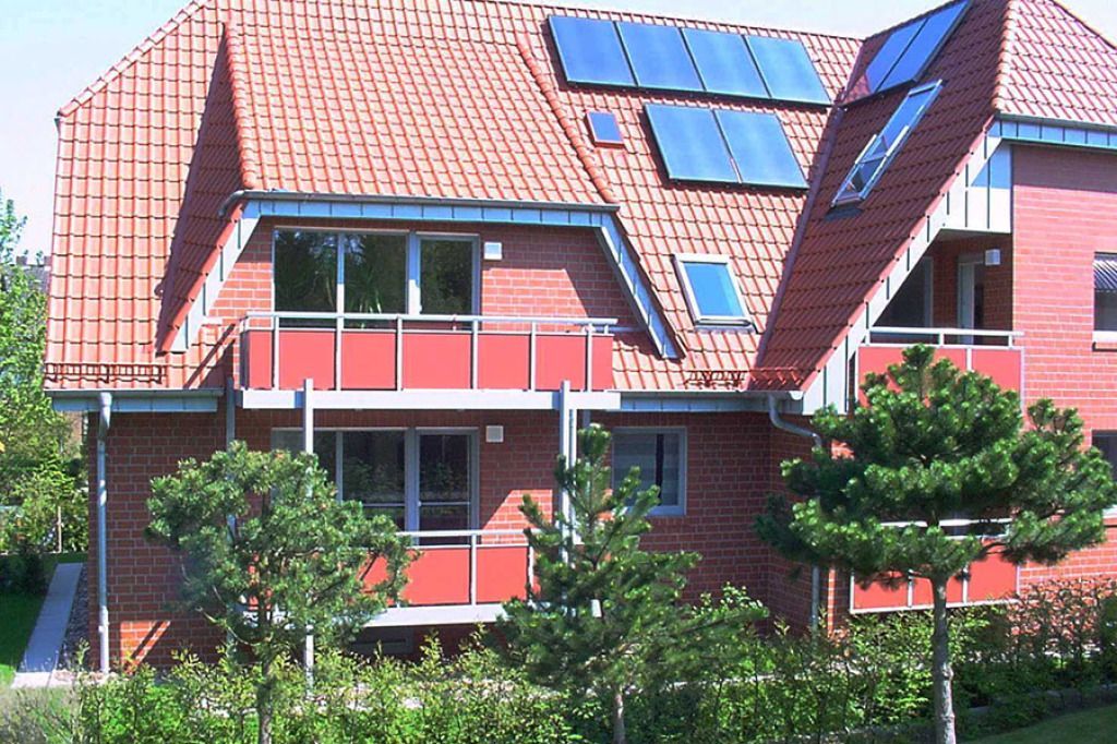 Rotes Backsteinhaus mit rotem Ziegeldach, Solarzellen, Balkonen und Grünflächen.