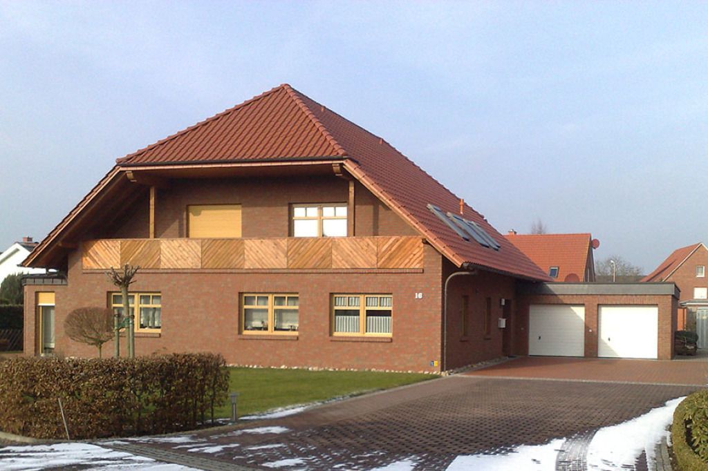 Backsteinhaus mit rotem Dach und Garage, umgeben von Schnee und Backsteinauffahrt.