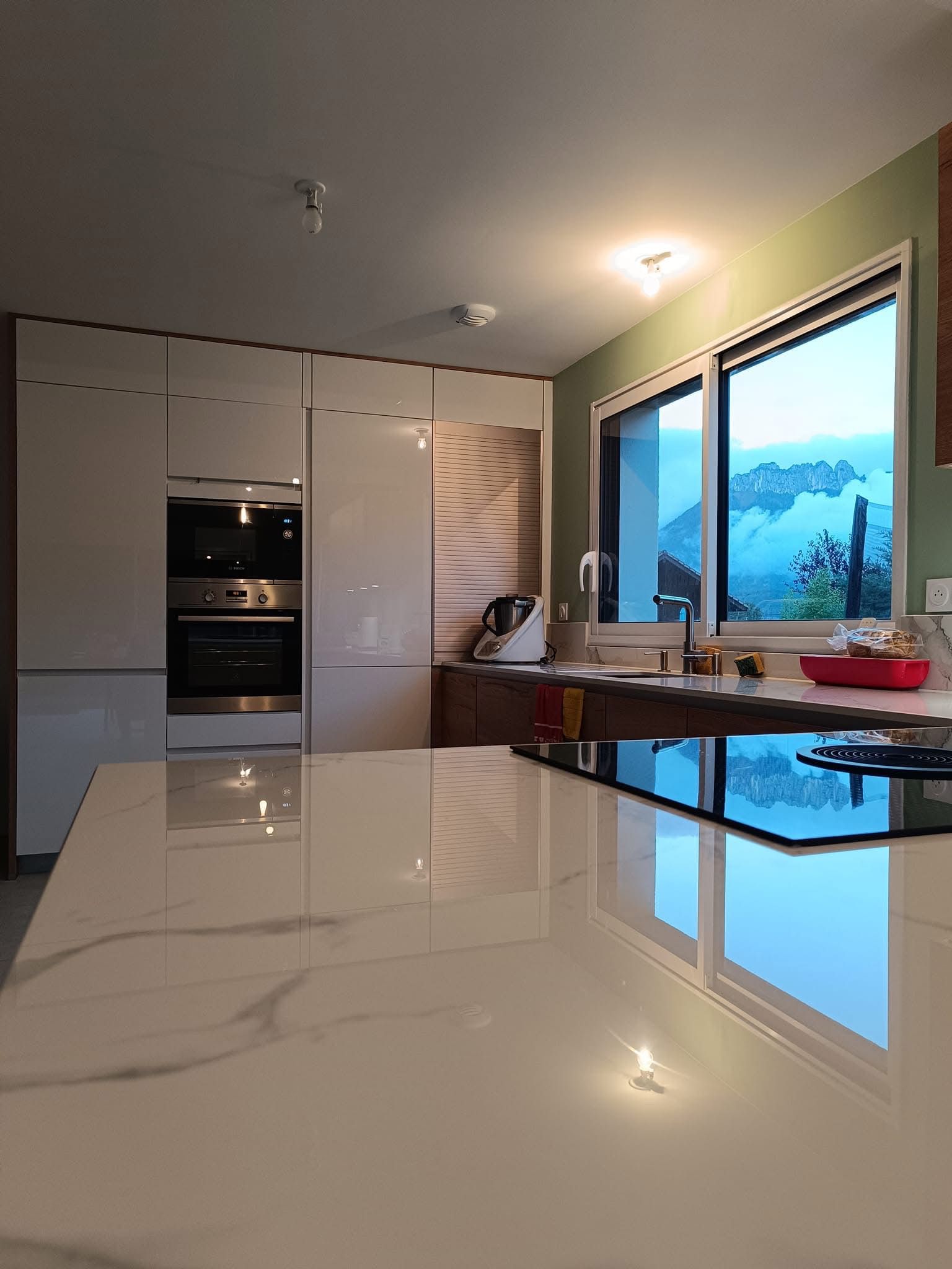 Cuisine moderne avec armoires, îlot central et fenêtre donnant sur la montagne.