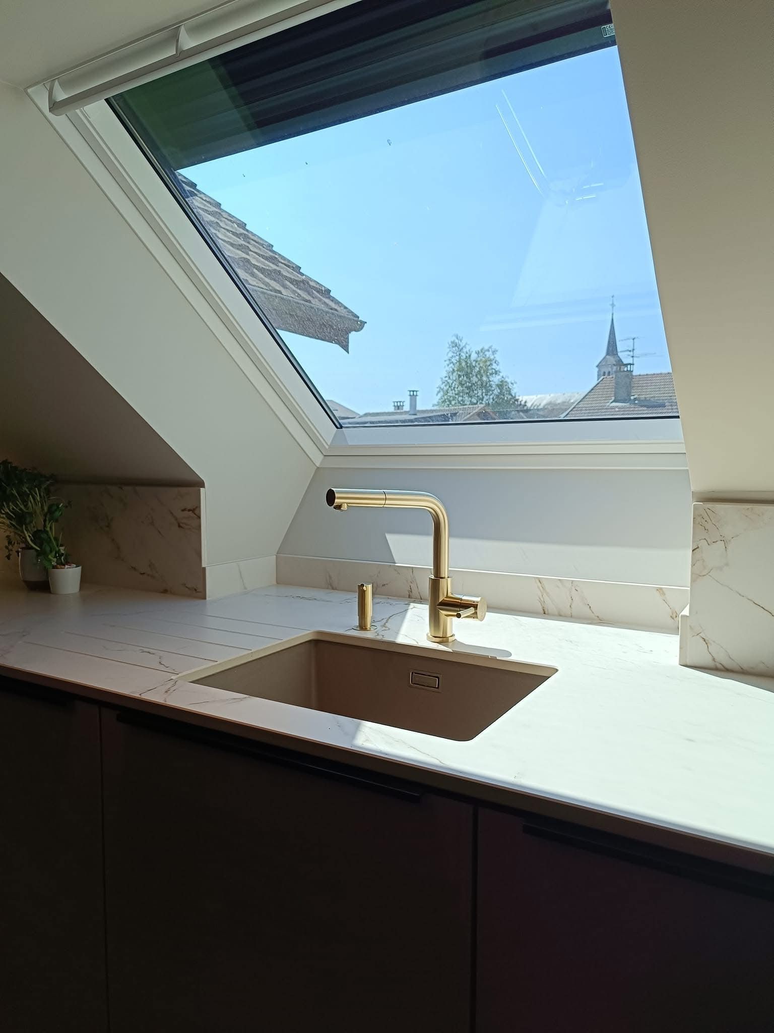 Évier de cuisine avec robinet, installé sous une verrière offrant une vue sur les toits.