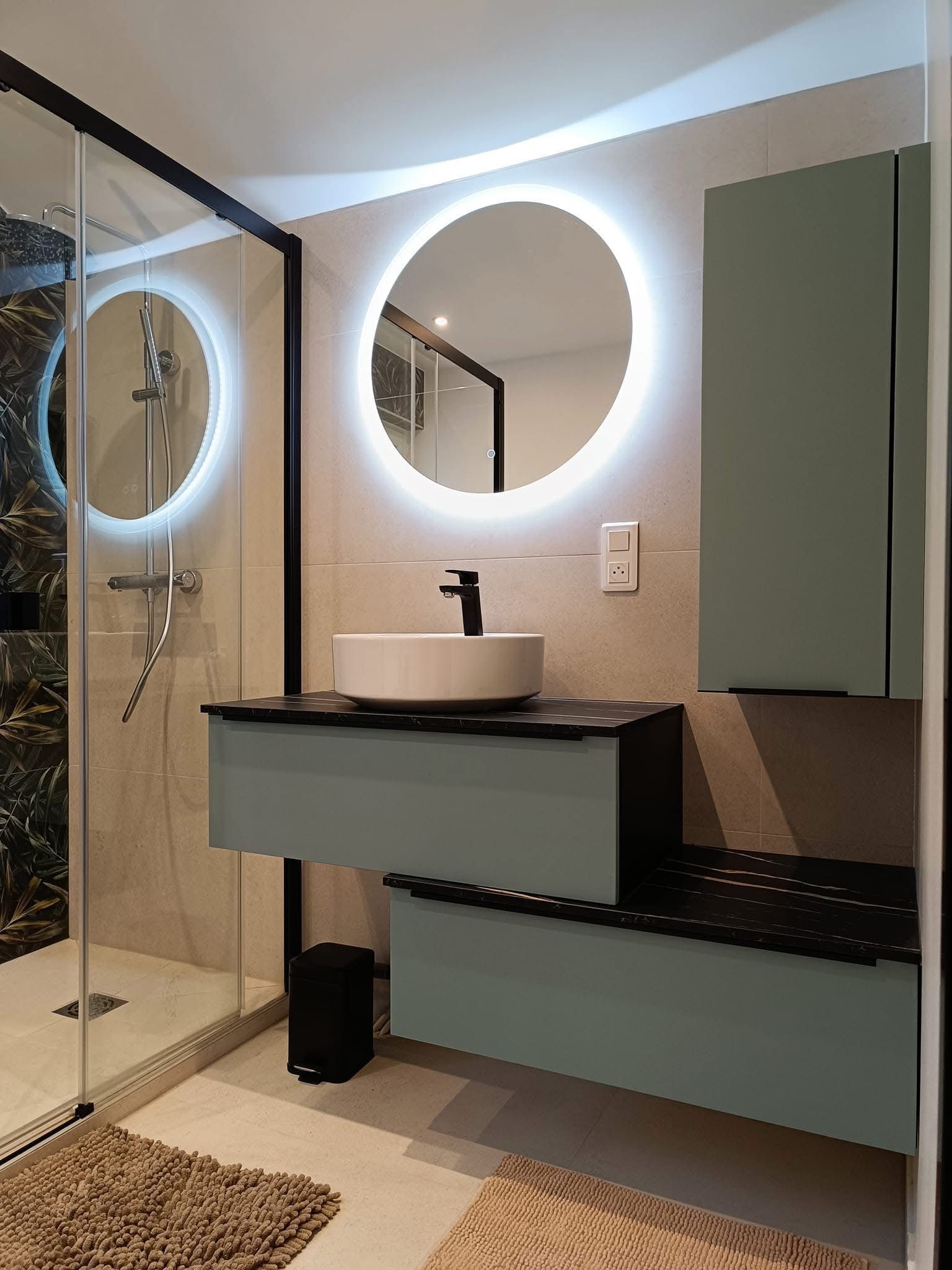 Salle de bains moderne avec un miroir rond éclairé, un meuble à lavabo suspendu avec vasque et une douche en verre.