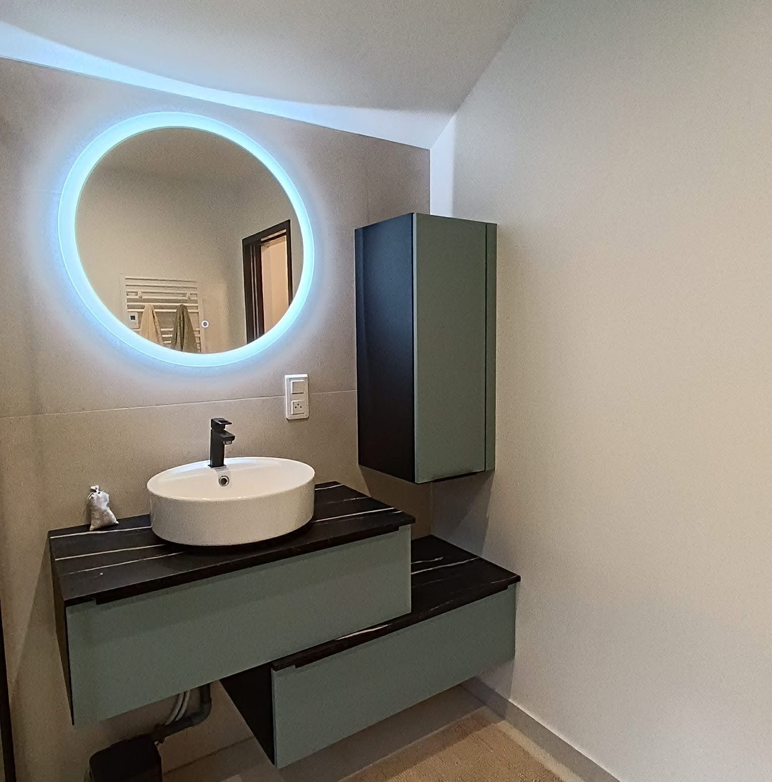 Salle de bains moderne avec miroir rond rétroéclairé, vasque et armoire de rangement murale.