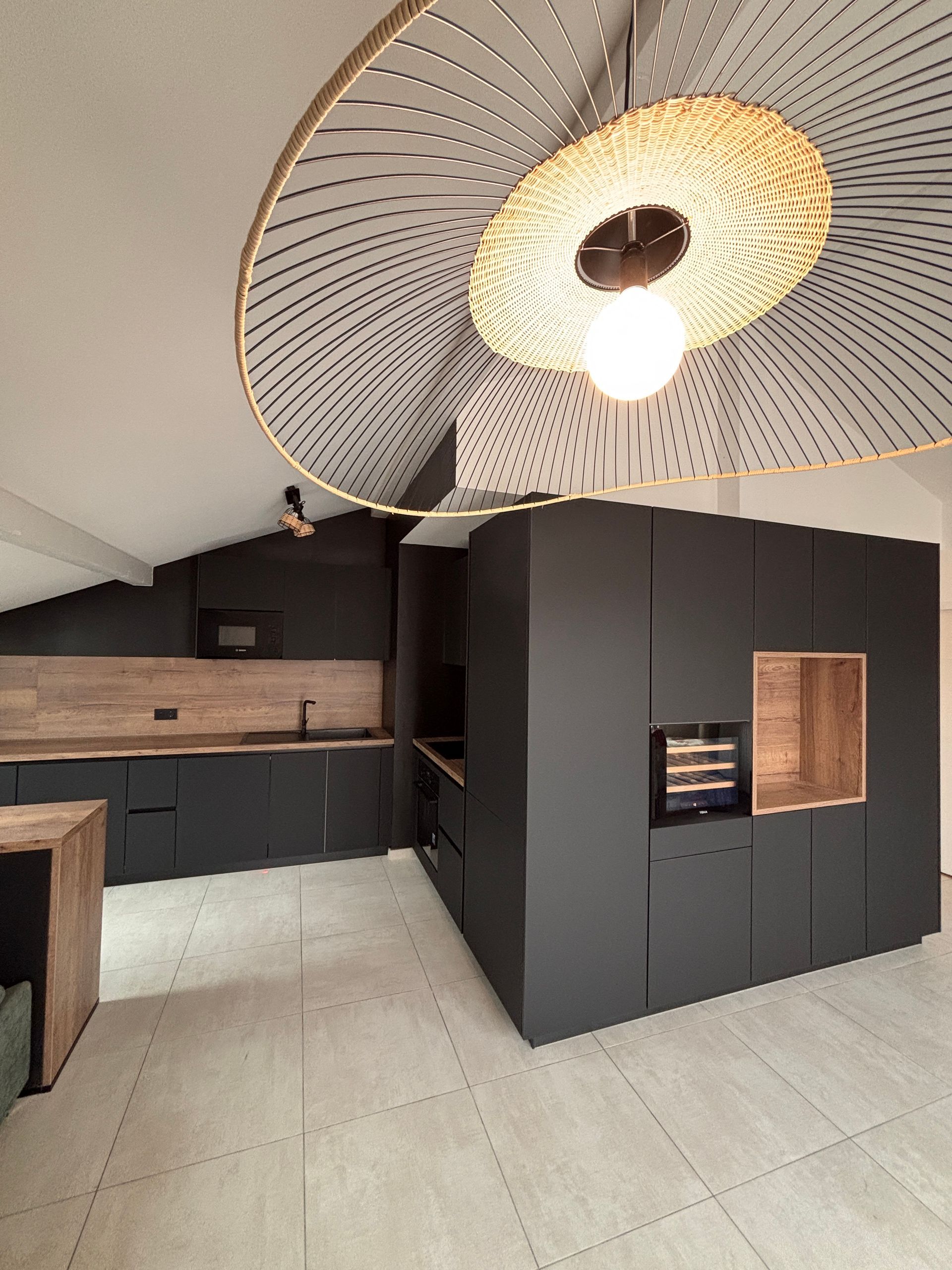 Cuisine moderne avec placards, éléments en bois et suspension lumineuse en tissu tressé.