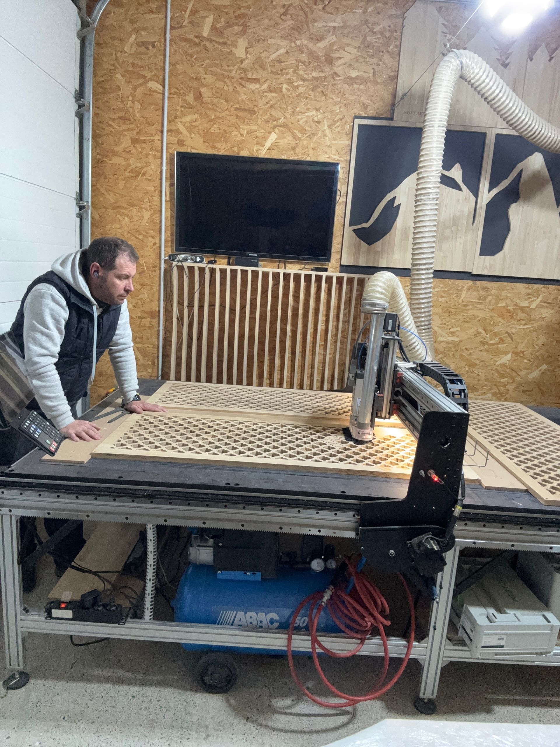 Homme utilisant une machine CNC pour découper du bois, environnement d'atelier.