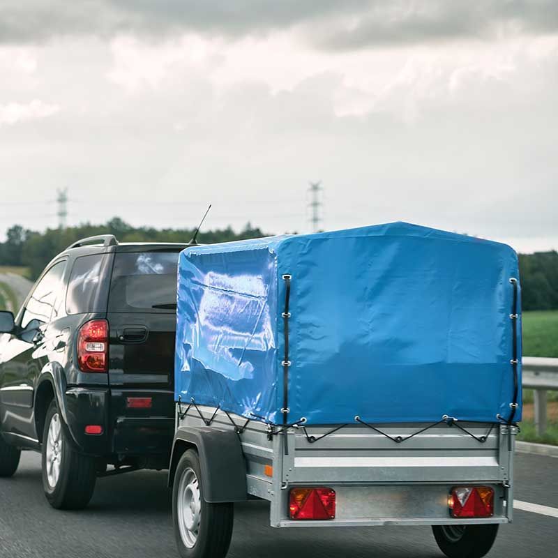 Schwarzer Geländewagen zieht einen Anhänger mit blauer Plane auf einer Straße.