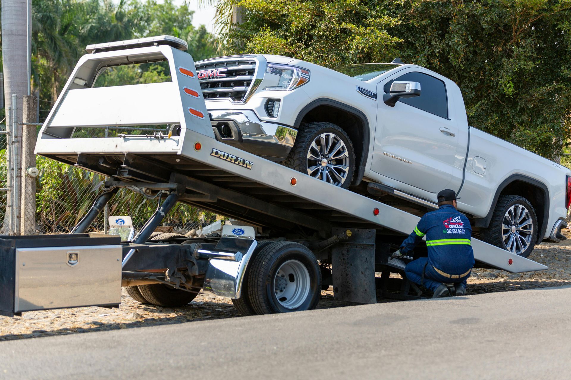 Ein weißer Pickup-Truck auf einem Abschleppwagen wird am Straßenrand von einer Person in blauer Uniform beladen.