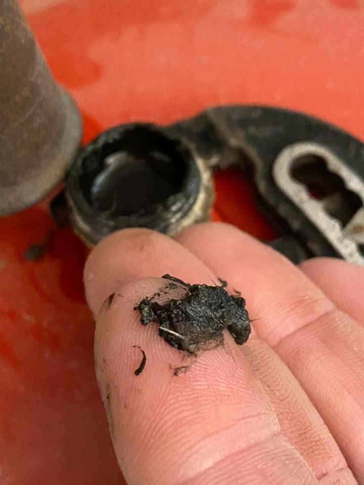 Un doigt tient une boule de graisse noire et granuleuse sur un fond flou 
