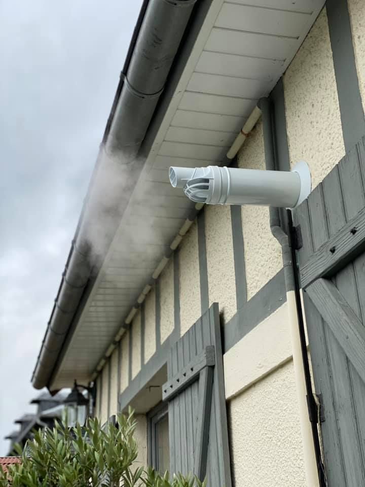 Une grille d'aération horizontale blanche, faisant saillie d'un mur clair d'un bâtiment, laisse échapper de la vapeur