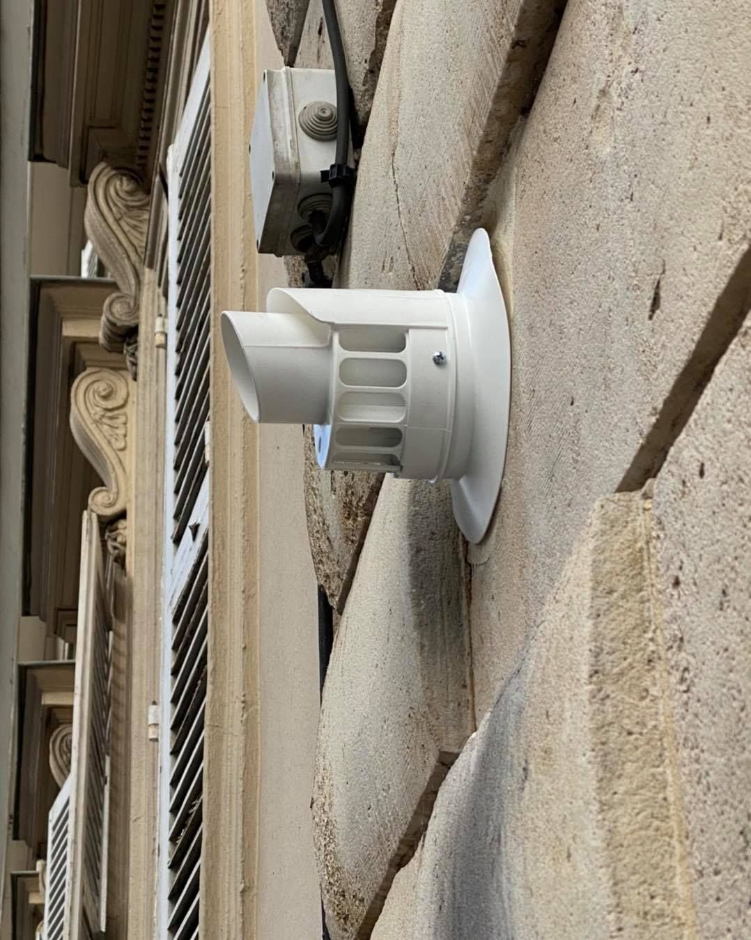 Une hotte aspirante en plastique blanc, fixée sur un mur extérieur en pierre beige