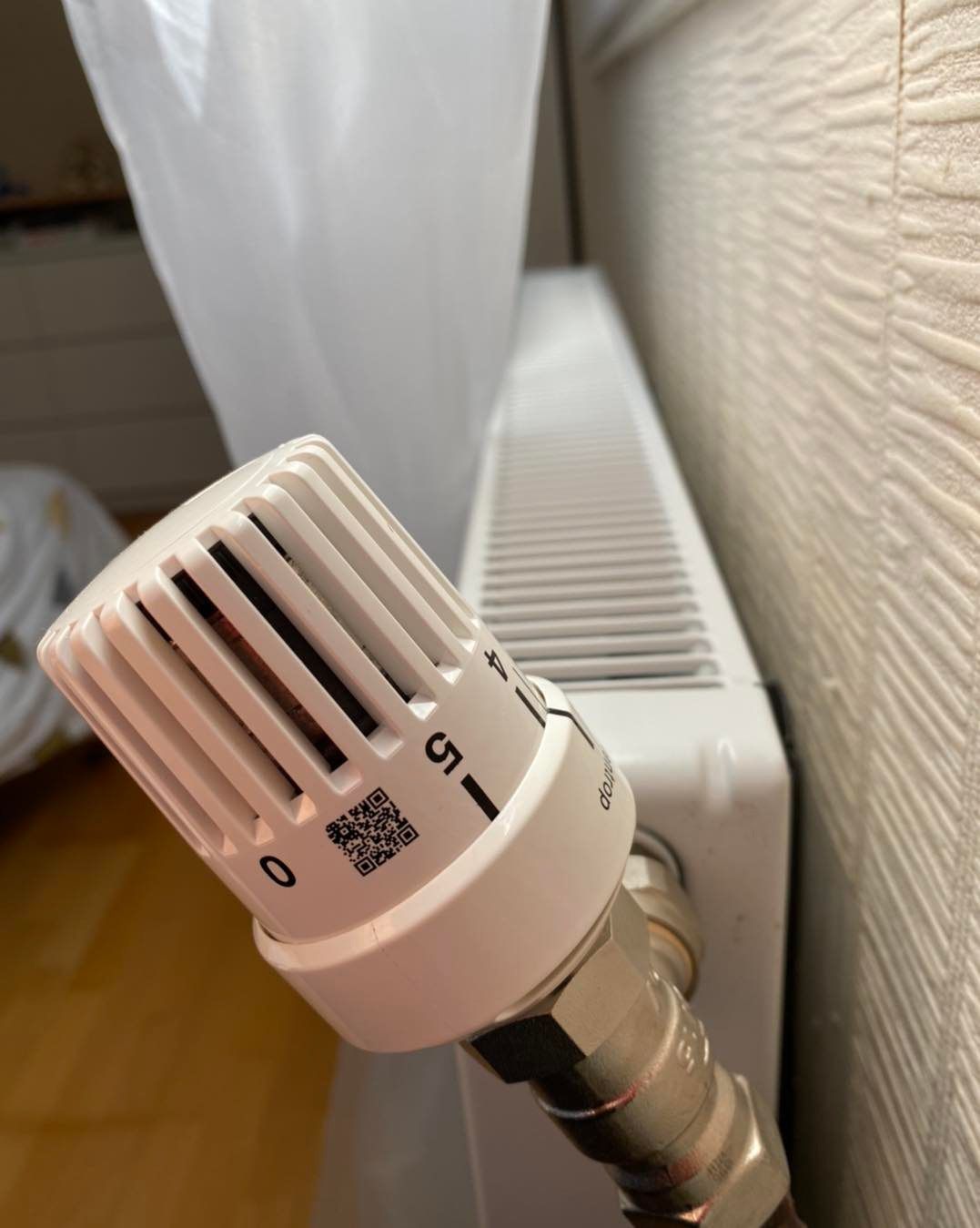 Gros plan sur le cadran blanc d'un thermostat de radiateur gradué de 0 à 5, placé près d'un radiateur contre un mur texturé.