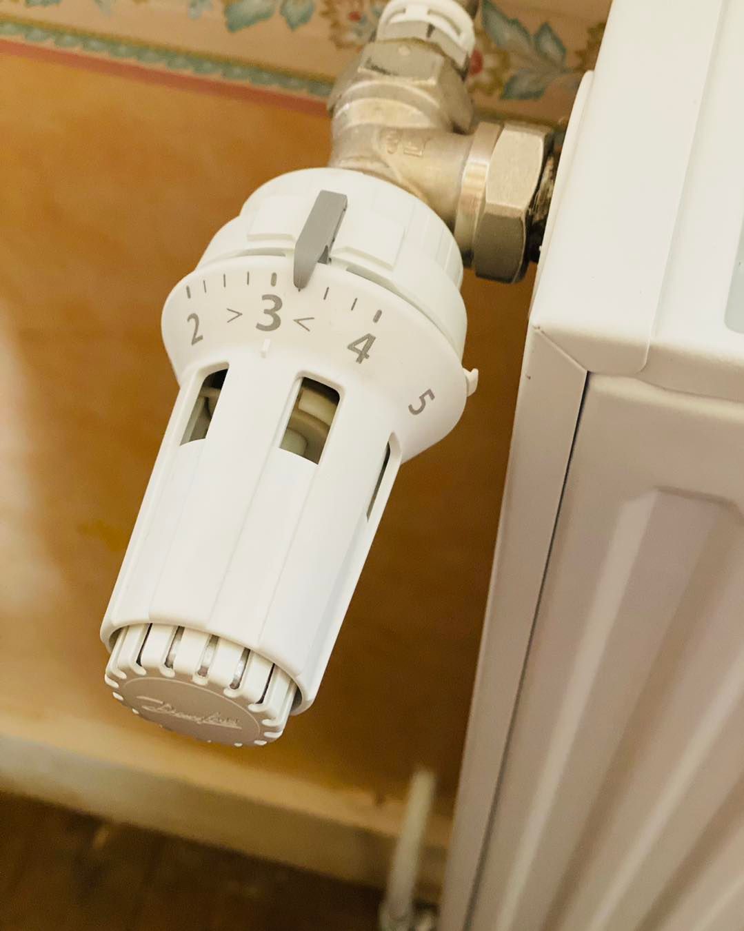 Un robinet thermostatique blanc pour radiateur, réglé sur la position trois, fixé à un radiateur mural.