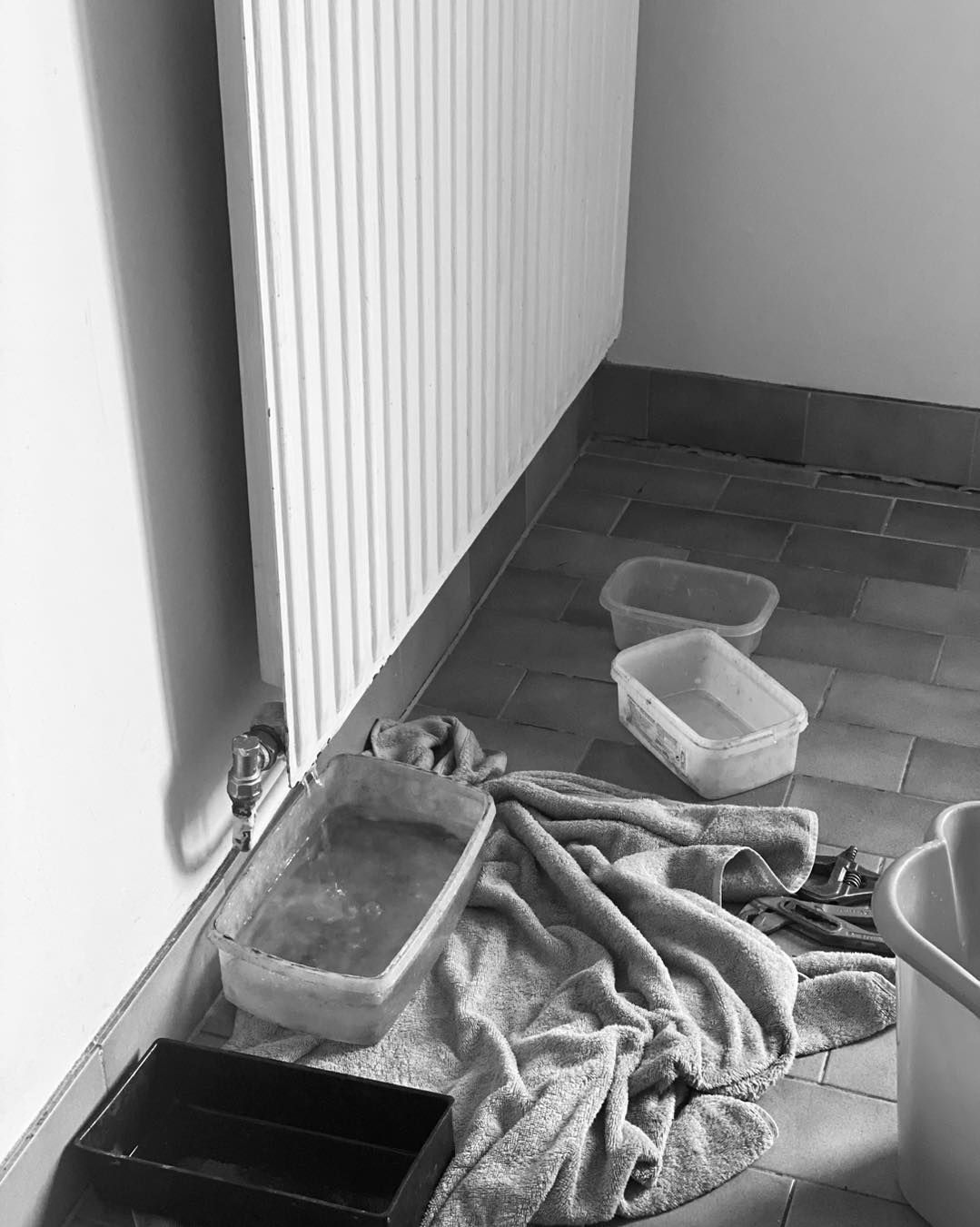 Un radiateur en cours de purge sur un sol carrelé, avec des récipients en plastique et une serviette placés en protection.